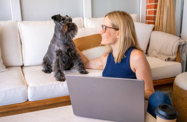 Köpeğiyle genç bir kadın evdeki terasta dizüstü bilgisayar kullanıyor..