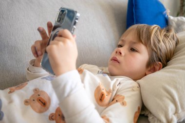 Evdeki akıllı telefonu kullanarak kanepede uzanan küçük çocuk..