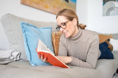 kitap okurken kanepede yatan kadın.