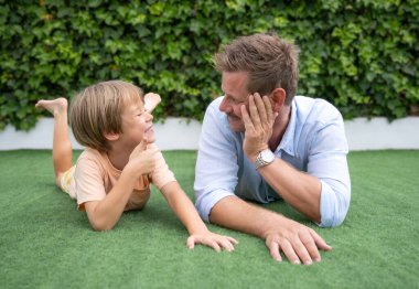 Neşeli bir çocuk ve babası evdeki çimlerin üzerinde yatıyor. Babalık kavramı.