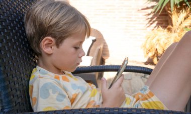 Açık bir sandalyede oturan akıllı telefon kullanan bir çocuğun profil görüntüsü.