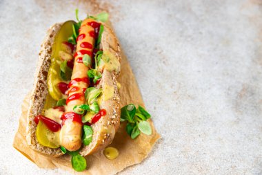 Sosisli sandviç, domates sosu, salatalık turşusu, yeşillik, marul, hazır yiyecek lezzetli taze yemek aperatifler masa arkasındakinin fotokopisi.