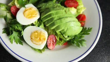 Salata avokado, haşlanmış yumurta, domates, yeşil yaprak marul, sebze tabağı taze lezzetli gurme yemek arkaplanı masa kırsal yiyeceklerin üst görünümü fotokopi alanı.