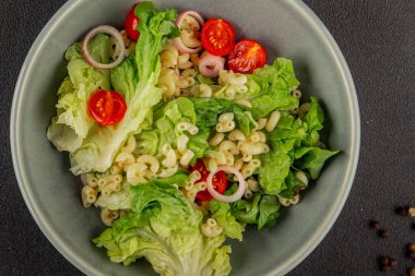 Makarna salatası yeşil yaprak marul, domates, makarna, soğan taze lezzetli gurme yemek arkaplan masa üzerinde rustik gıda üst görünüm fotokopi alanı keto ve paleo diyet vegan ve vejetaryen gıda