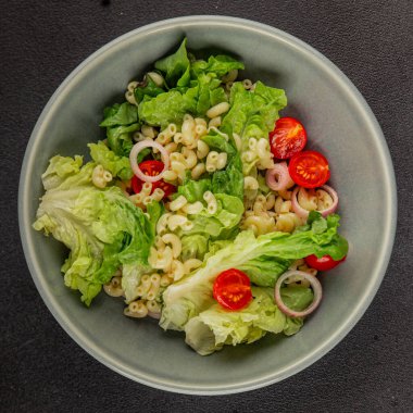 Makarna salatası yeşil yaprak marul, domates, makarna, soğan taze lezzetli gurme yemek arkaplan masa üzerinde rustik gıda üst görünüm fotokopi alanı keto ve paleo diyet vegan ve vejetaryen gıda