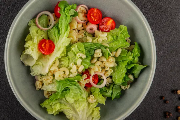 Makarna salatası yeşil yaprak marul, domates, makarna, soğan taze lezzetli gurme yemek arkaplan masa üzerinde rustik gıda üst görünüm fotokopi alanı keto ve paleo diyet vegan ve vejetaryen gıda