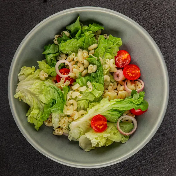 Makarna salatası yeşil yaprak marul, domates, makarna, soğan taze lezzetli gurme yemek arkaplan masa üzerinde rustik gıda üst görünüm fotokopi alanı keto ve paleo diyet vegan ve vejetaryen gıda