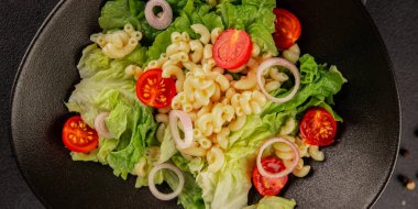 Makarna salatası yeşil yaprak marul, domates, makarna, soğan taze lezzetli gurme yemek arkaplan masa üzerinde rustik gıda üst görünüm fotokopi alanı keto ve paleo diyet vegan ve vejetaryen gıda