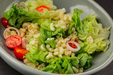 Makarna salatası yeşil yaprak marul, domates, makarna, soğan taze lezzetli gurme yemek arkaplan masa üzerinde rustik gıda üst görünüm fotokopi alanı keto ve paleo diyet vegan ve vejetaryen gıda