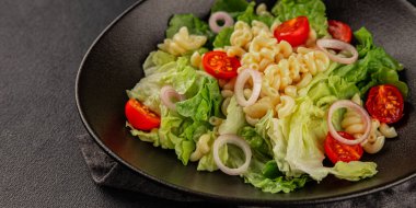 Makarna salatası yeşil yaprak marul, domates, makarna, soğan taze lezzetli gurme yemek arkaplan masa üzerinde rustik gıda üst görünüm fotokopi alanı keto ve paleo diyet vegan ve vejetaryen gıda