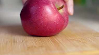 Bir ev aşçısı büyük bir kırmızı elmayı tahta bir tahtanın üzerinde bıçakla keser. Sağlıklı yeme, vejetaryenlik ve eko ürünleri kavramı