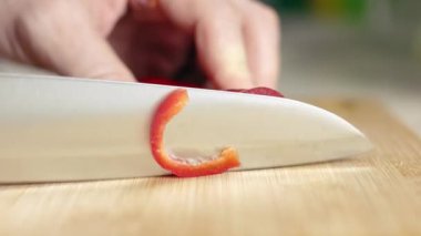 Bir ev aşçısı kırmızı biberi tahta bir tahtada bıçakla keser. Sağlıklı yeme, vejetaryenlik ve eko ürünleri kavramı