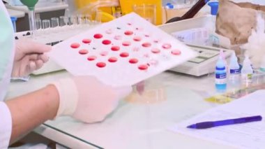 Beyaz önlüklü odaklanmış bir laboratuvar teknisyeni test tüpleri, bilimsel ekipmanlar ve numunelerle çevrili iyi donanımlı bir laboratuvar ortamında kan tahlilleri yapıyor..