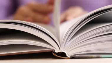 Bir elin nazikçe sayfalarını çevirdiği açık bir kitabın yakın plan görüntüsü, herhangi bir edebi tema için mükemmel