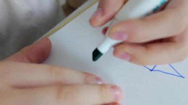 Genç bir çocuk boş bir kağıt üzerine çizim yapmak için yeşil ve mavi bir işaret kullanıyor.