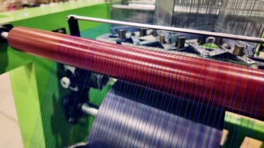 Bir tekstil makinesinin detaylı bir yakın çekim görüntüsü, iş yerindeki karmaşık makinelerle birlikte canlı renk rulolarını vurgular