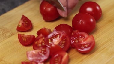 Canlı vişneli domatesler yemek pişirmek için kırsal bir ahşap yüzey üzerinde dikkatlice dilimleniyorlar.