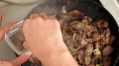 Bir el tavada sotelenmiş ete baharat ekliyor, mutfak teknikleri gösteriyor.