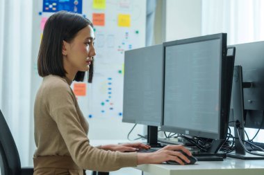 Ofiste bilgisayar monitörü önünde oturan Asyalı mühendis yazılım verileri ile kodlama uygulaması geliştirdi