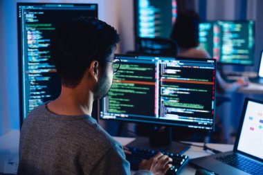 Modern ofiste geceleri kod ve uygulama diyagramlarını gösteren birden fazla ekran üzerinde çalışan Asyalı yazılım geliştiricileri