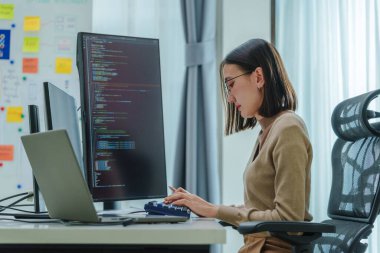 Ofiste bilgisayar monitörü önünde oturan Asyalı mühendis yazılım verileri ile kodlama uygulaması geliştirdi