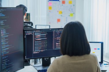 Modern bir ofiste kod ve uygulama diyagramları gösteren birden fazla ekran üzerinde çalışan Asyalı yazılım geliştiricileri