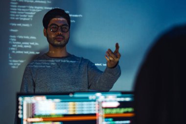 Hintli programcı, kod projeksiyonuyla ekranın önünde duruyor. Teknolojinin ve insan uzmanlığının yazılım geliştirme entegrasyonunu sunuyor.