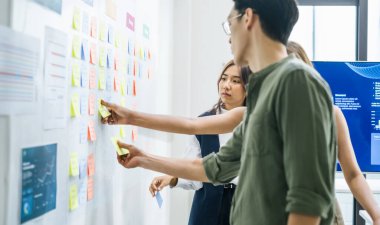 Modern bir ofiste fikir ve iş akışını düzenlemek için bir görev tahtasında (kanban) yapışkan notlar kullanarak beyin fırtınası oturumu