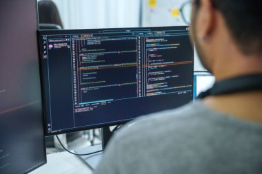 Modern bir ofiste kod ve uygulama diyagramları gösteren birden fazla ekran üzerinde çalışan Asyalı yazılım geliştiricileri