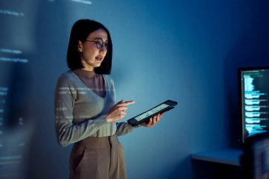 Asyalı kadın programcı kod projeksiyonlu ekranın önünde duruyor. Teknolojinin ve insan uzmanlığının yazılım geliştirme entegrasyonunu sunuyor.