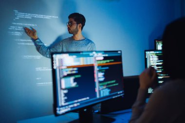 Hintli programcı, kod projeksiyonuyla ekranın önünde duruyor. Teknolojinin ve insan uzmanlığının yazılım geliştirme entegrasyonunu sunuyor.