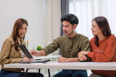 Çift müvekkil toplantısı sırasında tablet üzerinde dosya ve veri sunan Asyalı mali danışman. Finansal planlama ve karar verme