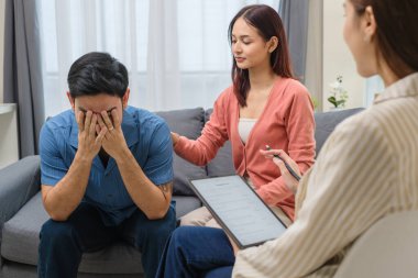 Bir çiftin terapi seansı sırasında üzgün Asyalı adam elleriyle yüzünü kapatıyor.