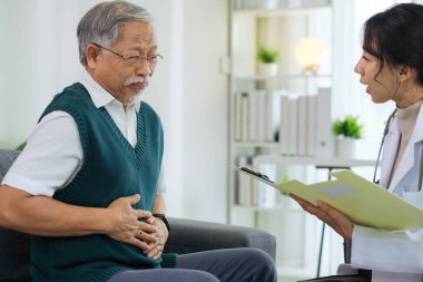 Doktor, sağlık muayenesi sırasında karın ağrısı olan kıdemli bir hastayla konuşuyor.