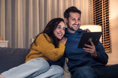 İspanyol çift dijital tablet kullanarak geceleri evdeki kanepede birlikte gösteri yapıyorlar.