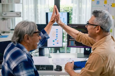 Kıdemli geliştirici ekibi modern bir bilgisayar çalışma istasyonunda yazılım işbirliği ve kodlamada başarıyı kutluyor