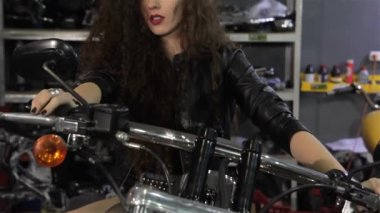 Genç kadın motosiklet motosiklet gaz tankı üzerinde onu dirsek tarafından yaslanmış. Seksi kıvırcık kız elini motosiklet Atölyesi'nde çenesinin koyarak kapatın. Siyah deri ceketli oldukça beyaz kadın