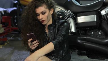 Çekici kadın motorcu motosiklet atölye helikopterde yakınındaki telefonda çağrı. Çok kıvırcık kız motosiklet yakın katta oturan kirli yanak ile kapatın. Genç Kafkas kadın