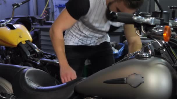 젊은은 오토바이 워크숍에서 Squating 매력적인 팔꿈치에 오토바이 좌석에 기대어 남자가 — 비디오