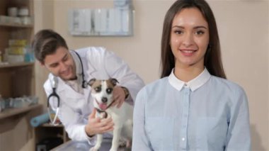 Veteriner Kliniği onaylama oldukça beyaz kız. Erkek veteriner holding köpek masada. Parmağını esmer erkek veteriner köpek ile arka plan karşı gösterilen genç gülümseyen kız