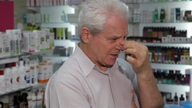 Üst düzey erkek müşteri eczanede kötü hissediyor. Beyaz adam burnunu gözler arasında masaj yaşlı. Eczaneden ilaç arayan eski gri adam
