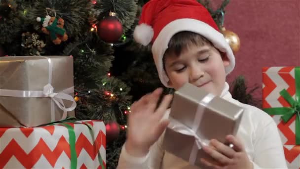 白人小男孩摇圣诞礼品盒 男性的孩子想知道什么样的内部的礼物盒附近圣诞树 小男孩检查银彩色的礼品盒 — 图库视频影像