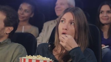Orta yaşlı kadın sinemada patlamış mısır yemek. İki genç kadın ve bir komuta sizde arka planı oturan orta yaşlı kadın.