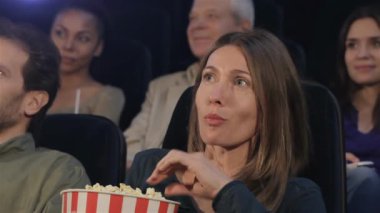 Çekici beyaz kadın sinema salonu, ağız patlamış mısır koyarak. Güzel bir kadın film izlerken ve patlamış mısır yemek gülüyor. Diğer arka plan üzerinde oturan orta yaşlı kadın