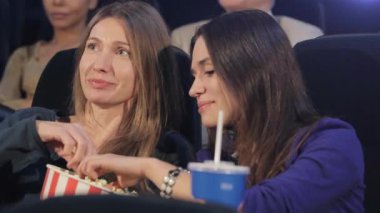 Güzel kız sinema womans Kova patlamış mısır alarak. Orta yaşlı kadın ve genç kadın yakın sinemada siting. İki kadın sinema filmi izlerken eğlenmek