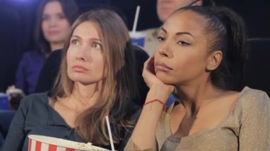Sinemada çenesini eline dayayan çekici siyahi kadın. Orta yaşlı beyaz kadın ve genç Afro-Amerikan kadın ciddi bir film izliyorlar. İki kadın çok endişeli.