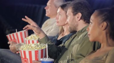 Sinemada kova ellerinde patlamış mısır ile tutarak Movigoers. Yan görünümü dört insan sinemada film izliyor. Tıraşsız beyaz adam elini ekranda işaret