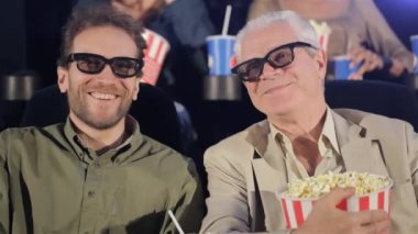 İki yetişkin adam film sinemasında 3D film izliyorum. Komuta sizde ve orta filmden gülen adam yaşlı. Gri saçlı yaşlı adam sinemada patlamış mısır yemek