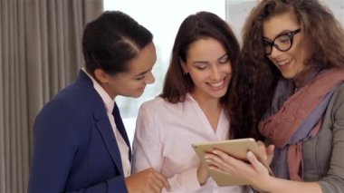 Ofisteki tablete bakan üç güzel kadın. Kafkasyalı kıvırcık kız elinde tablet tutuyor. Siyah kız ve beyaz kız işaret parmaklarını tablet ekranına doğrultuyor.