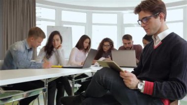 Ofiste çalışan genç yöneticilerinin yaratıcı ekibi. Beyaz adam bacakları tutarak bir başka bir katlanmış. Onun tableti dizlerinin üzerinde tutarak gözlük çekici esmer adam.